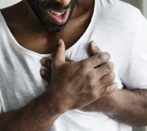 A person wearing a white shirt holds their chest with both hands, appearing to be in discomfort or pain, potentially indicating the need for primary care attention.