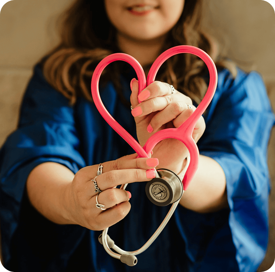 A person in a blue outfit holds a heart-shaped pink stethoscope close to their chest, embodying the essence of primary care, with their face partially visible.